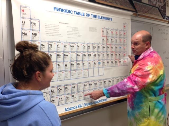 Mr. Christopher King shows a student the periodic table in his very own tye dye lab coat. 