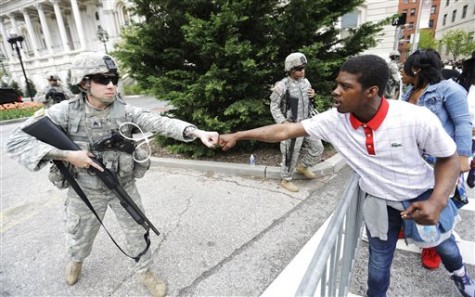 Brandon Payton, right, of Baltimore, fist-bumps a National Guardsman standing outside of City Hall as protesters march by to demonstrate the police-custody death of Freddie Gray, Thursday, April 30, 2015, in Baltimore. Baltimore police say they have turned over their criminal investigation to a prosecutor who will decide whether charges are warranted in the death of Gray. (AP Photo/David Goldman)