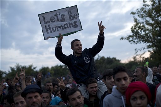 A man holds a sign reading Lets be Humans as he waits along with other migrants and refugees to be boarded onto buses, close to Croatias border with Serbia, in the town of Babska, Croatia, Wednesday, Sept. 23, 2015. European Union leaders will pledge to strengthen controls at the EUs borders with the outside world to help tackle the refugee crisis, according to a draft statement seen Wednesday by The Associated Press. (AP Photo/Marko Drobnjakovic)