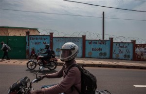 Men on motorbikes ride past a wall with a messages painted on it reading  'We go wash Ebola'  forming part of Sierra Leone's Ebola free campaign in the city of  Freetown, Sierra Leone, Friday, Jan. 15, 2016. A corpse has tested positive for Ebola in Sierra Leone, an official said Friday, the day after the World Health Organization declared the outbreak over in West Africa.  