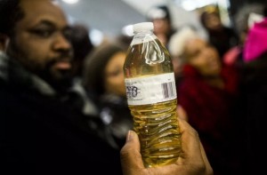 A Pastor holds up a bottle of Flint water as Michigan State Police hold a barrier to keep protesters out of the Romney Building, where Gov. Rick Snyder’s office resides on Thursday, Jan. 14, 2016, in Lansing, Mich. (Jake May/ AP Images)