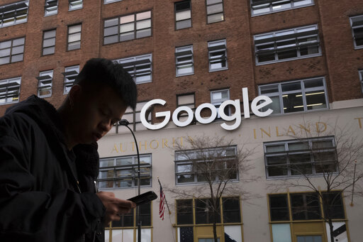 FILE - In this Dec. 17, 2018, file photo a man using a mobile phone walks past Google offices in New York. Google says it plans to launch a video-game streaming platform called Stadia, positioning itself to take on the traditional video-game business. (AP Photo/Mark Lennihan, File)