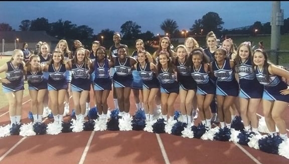 The cheerleading team poses for a picture in the football stadium.