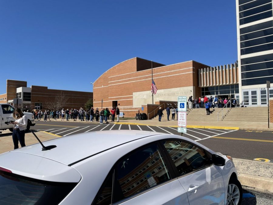 Just before entering the school, lines of people check into their vaccination appointments. 