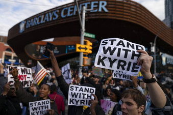 FILE - Protesters rallying against COVID-19 vaccination mandates and in support of basketball player Kyrie Irving gather in the street outside the Barclays Center before an NBA basketball game between the Brooklyn Nets and the Charlotte Hornets, Sunday, Oct. 24, 2021, in New York. From the NBAs Kyrie Irving missing the first months of the Brooklyn Nets season before making a partial return, to the NFLs Aaron Rodgers going from revered veteran to polarizing figure, to a diplomatic standoff over tennis star Novak Djokovics exemption to play in the Australian Open, sports figures have found themselves cheered and jeered as the most famous faces in fights over vaccine mandates and refusals. (AP Photo/John Minchillo, File)