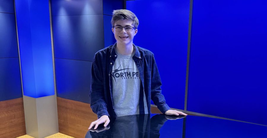 Ryan Bell standing at the desk of NPTV, at the studio where he produces content for North Penn High School