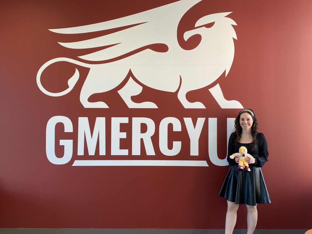 Professor Maddie Herman in University Hall at Gywnedd Mercy University holding mascot Merv.